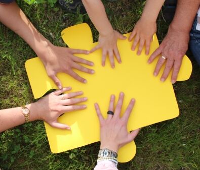 Hände verschiedener Generationen halten ein großen Puzzelteil fest